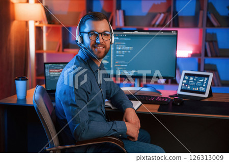 Positive professional programmer is working indoors and smiling. Neon lighting Positive professional programmer is working indoors and smiling. Neon lighting 126313009