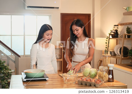 Mother and teenage daughter preparing a healthy meal together in a warm kitchen Mother and teenage daughter preparing a healthy meal together in a warm kitchen 126313419