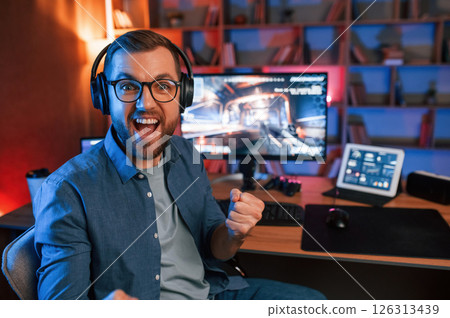 Celebrating victory. Man is playing the shooter game on his computer. Neon lighting 126313439