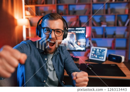 Celebrating victory. Man is playing the shooter game on his computer. Neon lighting 126313443