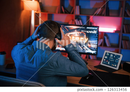 Man is playing the shooter game on his computer. Neon lighting 126313456