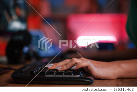 Close up view of woman's hand that is typing on the keyboard in dark room with neon lighting Close up view of woman's hand that is typing on the keyboard in dark room with neon lighting 126313468