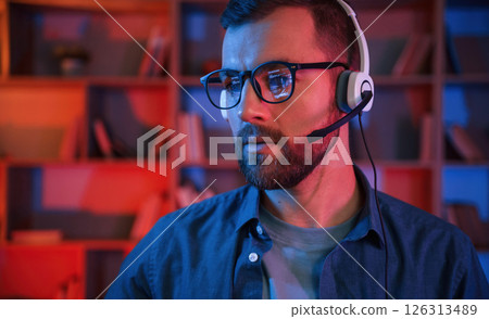 Portrait of man that is sitting by a computer indoors at home. Neon lighting Portrait of man that is sitting by a computer indoors at home. Neon lighting 126313489