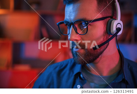Portrait of man that is sitting by a computer indoors at home. Neon lighting Portrait of man that is sitting by a computer indoors at home. Neon lighting 126313491