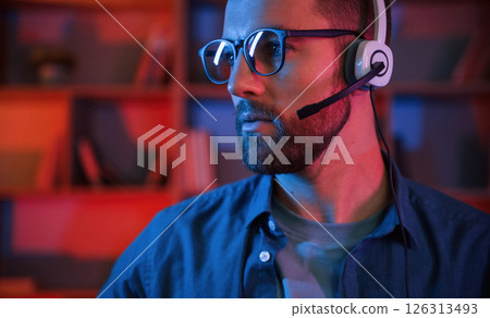 Man is sitting by a computer indoors at home. Neon lighting Man is sitting by a computer indoors at home. Neon lighting 126313493