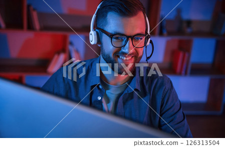 Read and blue neon lighting. Man is sitting by a computer indoors at home 126313504