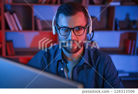 Read and blue neon lighting. Man is sitting by a computer indoors at home 126313506