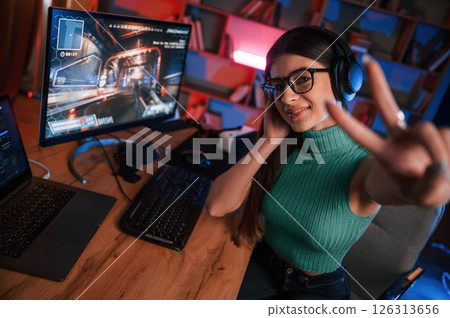 In headphones. Young pretty female gamer is playing shooter. Neon lighting In headphones. Young pretty female gamer is playing shooter. Neon lighting 126313656