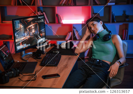 In headphones. Young pretty female gamer is playing shooter. Neon lighting In headphones. Young pretty female gamer is playing shooter. Neon lighting 126313657