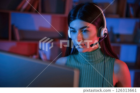Young woman in headphones is sitting by a pc. Neon lighting 126313661