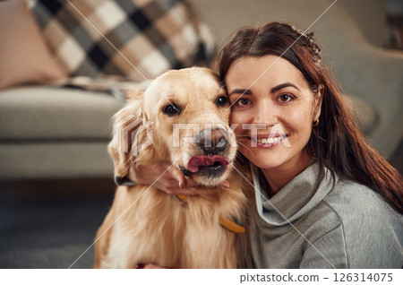 Looking at the camera. Woman is with golden retriever dog at home 126314075
