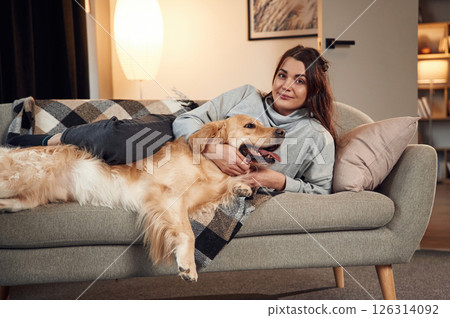 Lying down on the sofa together. Woman is with golden retriever dog at home 126314092