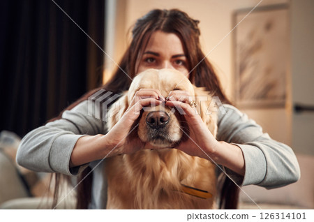 Covering face with hands. Love gesture. Woman is with golden retriever dog at home 126314101