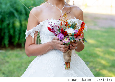 Bride with white wedding dress in forest holding colorful and dried wedding bouquet. Bride with white wedding dress in forest holding colorful and dried wedding bouquet. 126314155