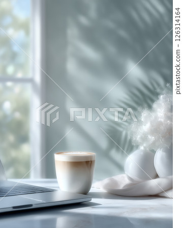 A minimalist workspace with a sleek silver laptop sitting on a white desk, next to a simple white ceramic coffee cup. 126314164