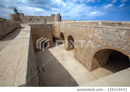 Castello maniace archways and defensive walls bathed in sunlight with lighthouse and blue sky in ortigia, syracuse, sicily, italy 126314432