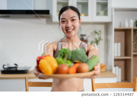Fit woman enjoys healthy fresh vegetables and fruits breakfast sitting in the kitchen. Fit woman enjoys healthy fresh vegetables and fruits breakfast sitting in the kitchen. 126314487