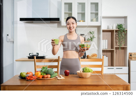 Fit woman enjoys healthy fresh vegetables and fruits breakfast sitting in the kitchen. 126314500