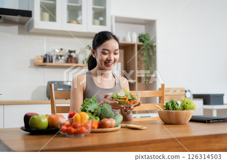 Fit woman enjoys healthy fresh vegetables and fruits breakfast sitting in the kitchen. Fit woman enjoys healthy fresh vegetables and fruits breakfast sitting in the kitchen. 126314503