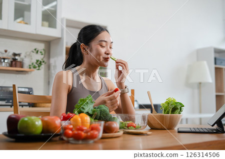 Fit woman enjoys healthy fresh vegetables and fruits breakfast sitting in the kitchen. 126314506
