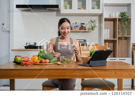 Fit woman enjoys healthy fresh vegetables and fruits breakfast sitting in the kitchen. 126314507