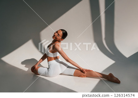 Yoga exercises on the floor. Beautiful sunlight. Young caucasian woman with slim body shape is indoors in the studio Yoga exercises on the floor. Beautiful sunlight. Young caucasian woman with slim body shape is indoors in the studio 126314574