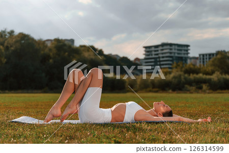 Side view. Doing yoga. Young caucasian woman with slim body shape is in the fitness clothes outdoors 126314599