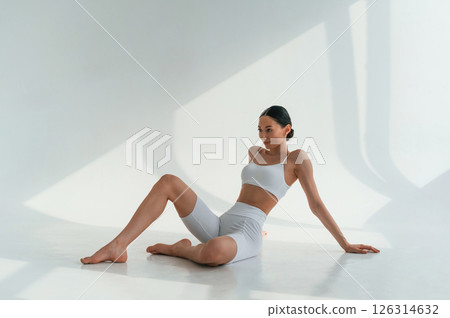 Relaxed, sitting on the floor. Young caucasian woman with slim body shape is indoors in the studio Relaxed, sitting on the floor. Young caucasian woman with slim body shape is indoors in the studio 126314632