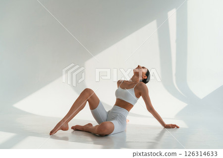 Relaxed, sitting on the floor. Young caucasian woman with slim body shape is indoors in the studio Relaxed, sitting on the floor. Young caucasian woman with slim body shape is indoors in the studio 126314633