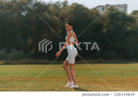 Walking on the field. Young caucasian woman with slim body shape is in the fitness clothes outdoors Walking on the field. Young caucasian woman with slim body shape is in the fitness clothes outdoors 126314634