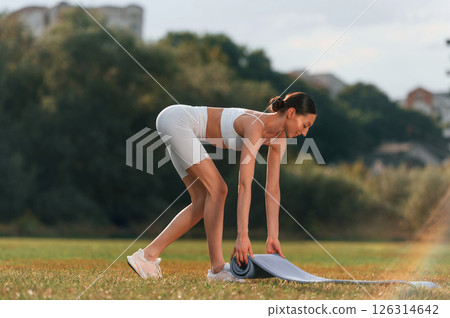 Rolling off the yoga mat. Young caucasian woman with slim body shape is in the fitness clothes outdoors Rolling off the yoga mat. Young caucasian woman with slim body shape is in the fitness clothes outdoors 126314642