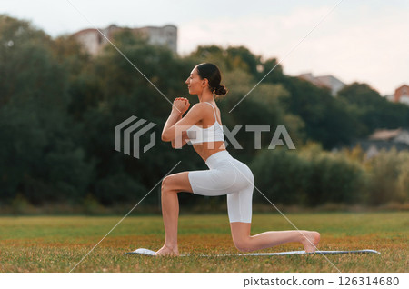 Doing squats. Young caucasian woman with slim body shape is in the fitness clothes outdoors 126314680