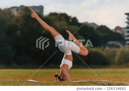 Head stand exercise. Young caucasian woman with slim body shape is in the fitness clothes outdoors 126314682