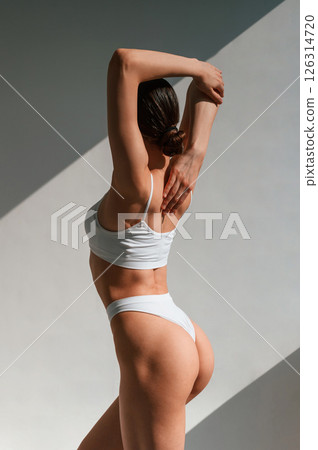 Showing the back. Young caucasian woman with slim body shape is indoors in the studio 126314720