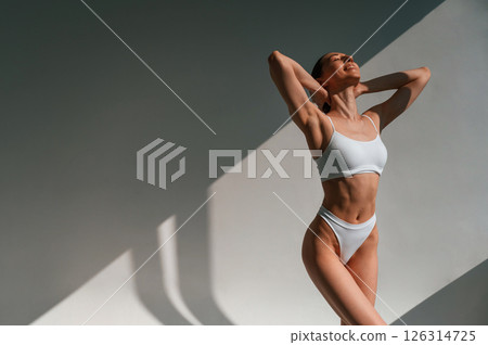 Feeling good, enjoying warmth of the sunlight. Young caucasian woman with slim body shape is indoors in the studio 126314725