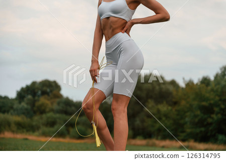 Yellow colored jumping rope. Young caucasian woman with slim body shape is in the fitness clothes outdoors 126314795