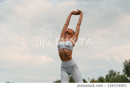 Warm up exercises. Young caucasian woman with slim body shape is in the fitness clothes outdoors 126314801