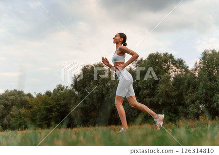 Running, everyday sport routine. Young caucasian woman with slim body shape is in the fitness clothes outdoors Running, everyday sport routine. Young caucasian woman with slim body shape is in the fitness clothes outdoors 126314810