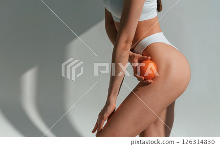 Fresh orange in hand. Young caucasian woman with slim body shape is indoors in the studio Fresh orange in hand. Young caucasian woman with slim body shape is indoors in the studio 126314830