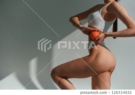 Fresh orange in hands. Young caucasian woman with slim body shape is indoors in the studio Fresh orange in hands. Young caucasian woman with slim body shape is indoors in the studio 126314832