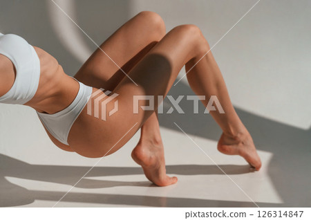 On the floor. View of legs and fitness body type. Young caucasian woman is indoors in the studio 126314847