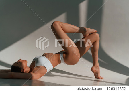 Peaceful mood. Lying down on the floor. Young caucasian woman with slim body shape is indoors in the studio Peaceful mood. Lying down on the floor. Young caucasian woman with slim body shape is indoors in the studio 126314852