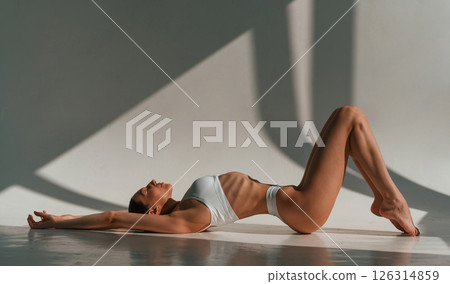 Peaceful mood. Lying down on the floor. Young caucasian woman with slim body shape is indoors in the studio Peaceful mood. Lying down on the floor. Young caucasian woman with slim body shape is indoors in the studio 126314859