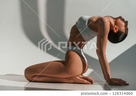 Exercise for the spine. Young caucasian woman with slim body shape is indoors in the studio Exercise for the spine. Young caucasian woman with slim body shape is indoors in the studio 126314860