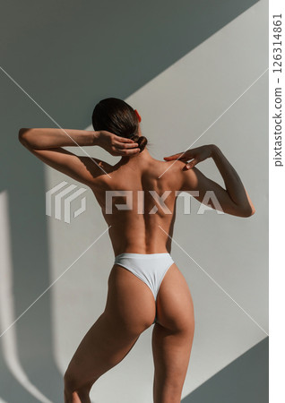Without bra. Showing back. Young caucasian woman with slim body shape is indoors in the studio Without bra. Showing back. Young caucasian woman with slim body shape is indoors in the studio 126314861