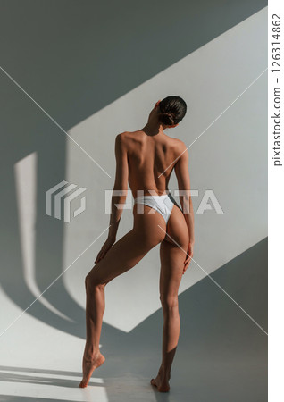 Without bra. Showing back. Young caucasian woman with slim body shape is indoors in the studio 126314862