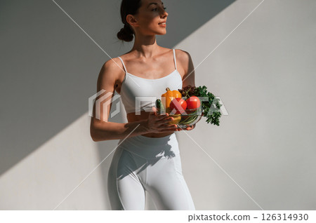 Holding vegetables and fruits. Young caucasian woman with slim body shape is indoors in the studio 126314930