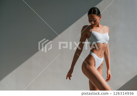 Standing against the wall and showing body. Young caucasian woman is indoors in the studio 126314936