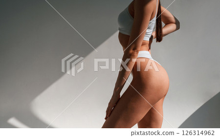 Against wall. Young caucasian woman with slim body shape is indoors in the studio Against wall. Young caucasian woman with slim body shape is indoors in the studio 126314962