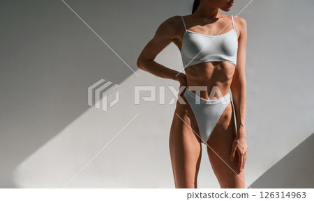Against wall. Young caucasian woman with slim body shape is indoors in the studio Against wall. Young caucasian woman with slim body shape is indoors in the studio 126314963